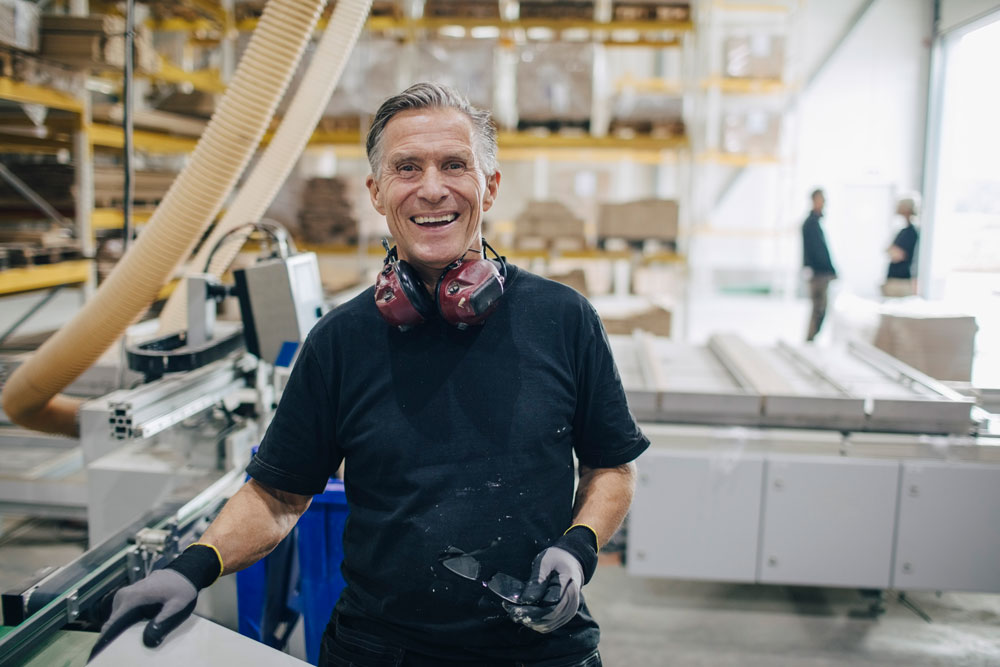 En leende arbetare som står vid en maskin inom timmer industrin.