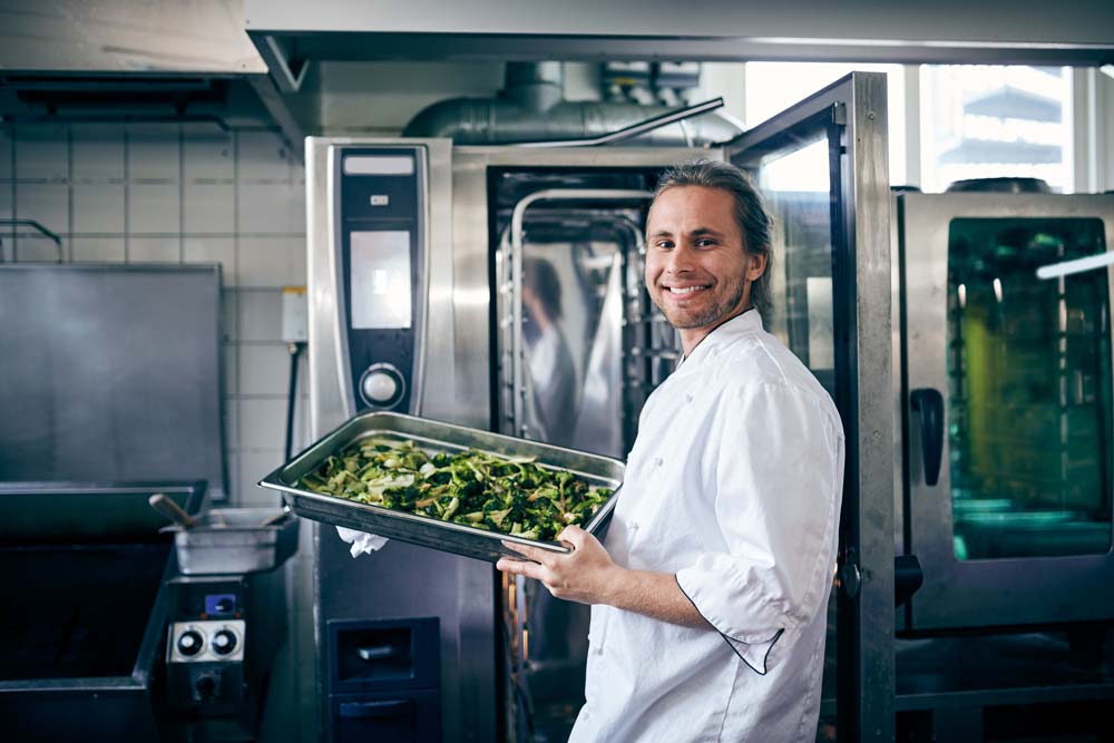 Man som står i ett restaurangkök och ler