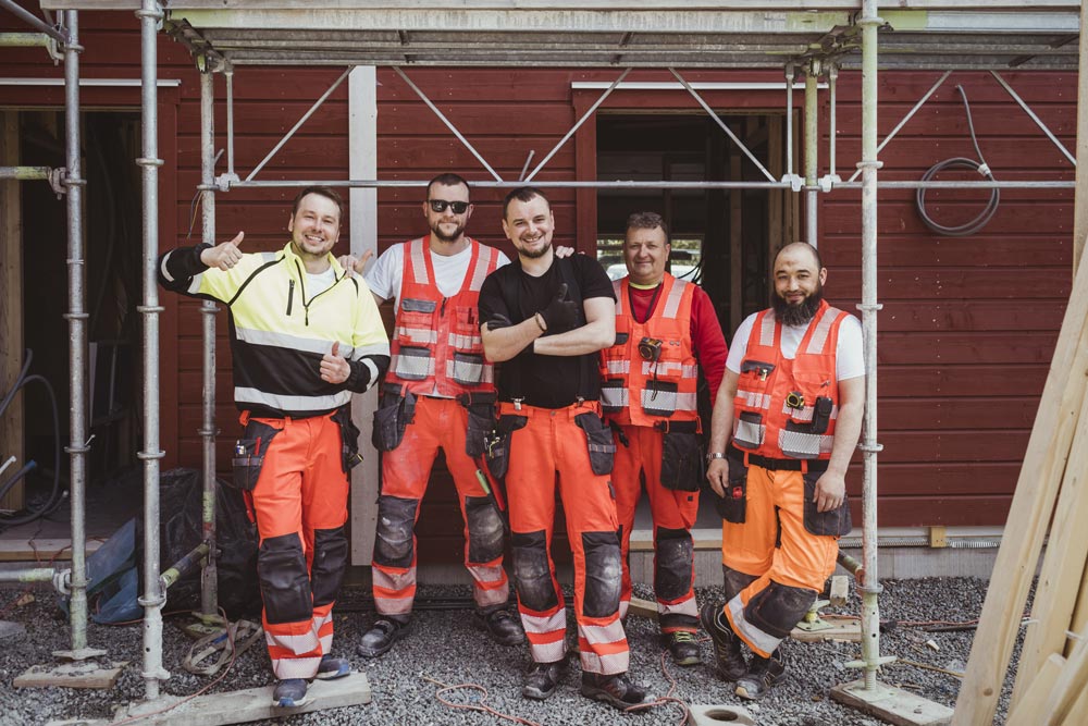 Fem byggarbetare i säkerhetsvästar under en byggställning.